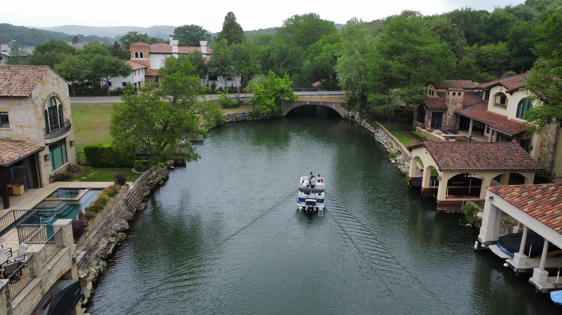 Pontoon boat cruising a Lake Austin canal lined with luxury waterfront homes